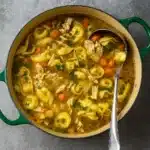 Chicken Tortellini Soup in a rustic bowl on a wooden table.